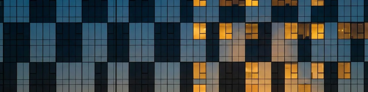 Modern office building at dusk with half the windows illuminated and half dark, representing workforce transformation